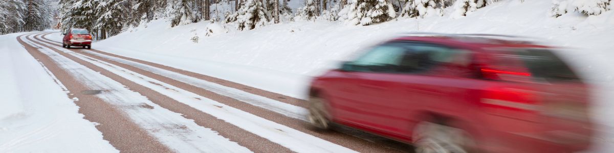 Red car speeding on a snowy, curving road, highlighting the dangers of excessive speed during winter holiday travel.