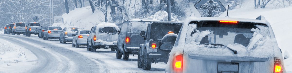 Cars driving cautiously on a snowy road surrounded by a winter landscape, emphasizing the importance of safe travel during holiday traffic.