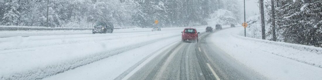 Cars navigating a snowy highway, representing safe driving habits for icy and snowy winter conditions.