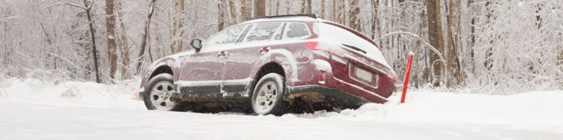 A vehicle stuck in snow in a forested area, highlighting essential tips for staying safe when stranded during winter travel.